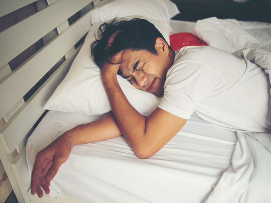 A person waking up in the morning looking grumpy, clearly not well-rested. The room is lit with natural light, but the mood reflects the struggle of waking up without a good night’s sleep