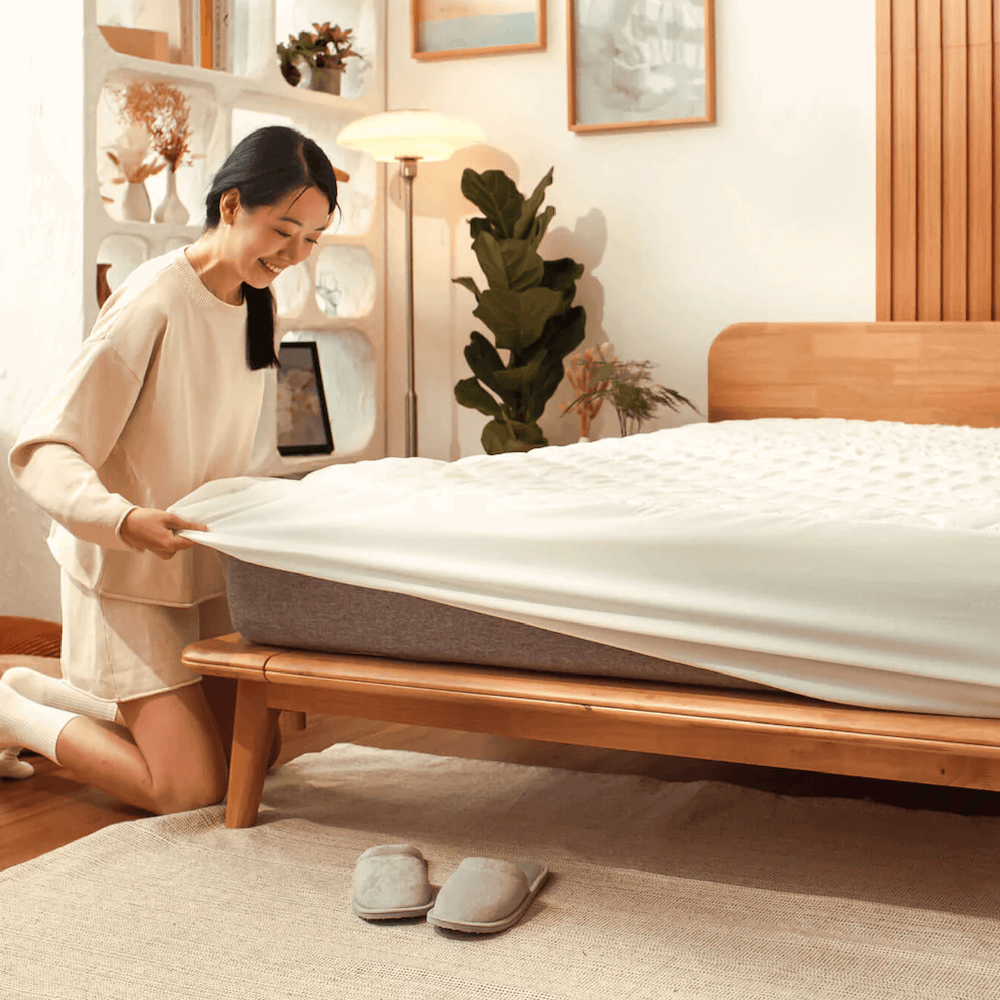 Woman placing Sonno waterproof mattress protector on bed for ultimate spill and allergen protection